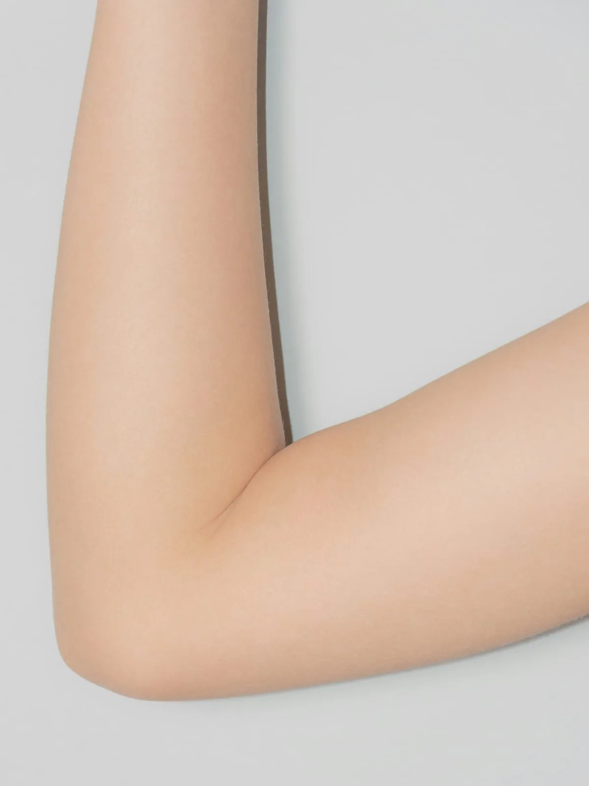 A bare arm bent at the elbow against a pale grey background