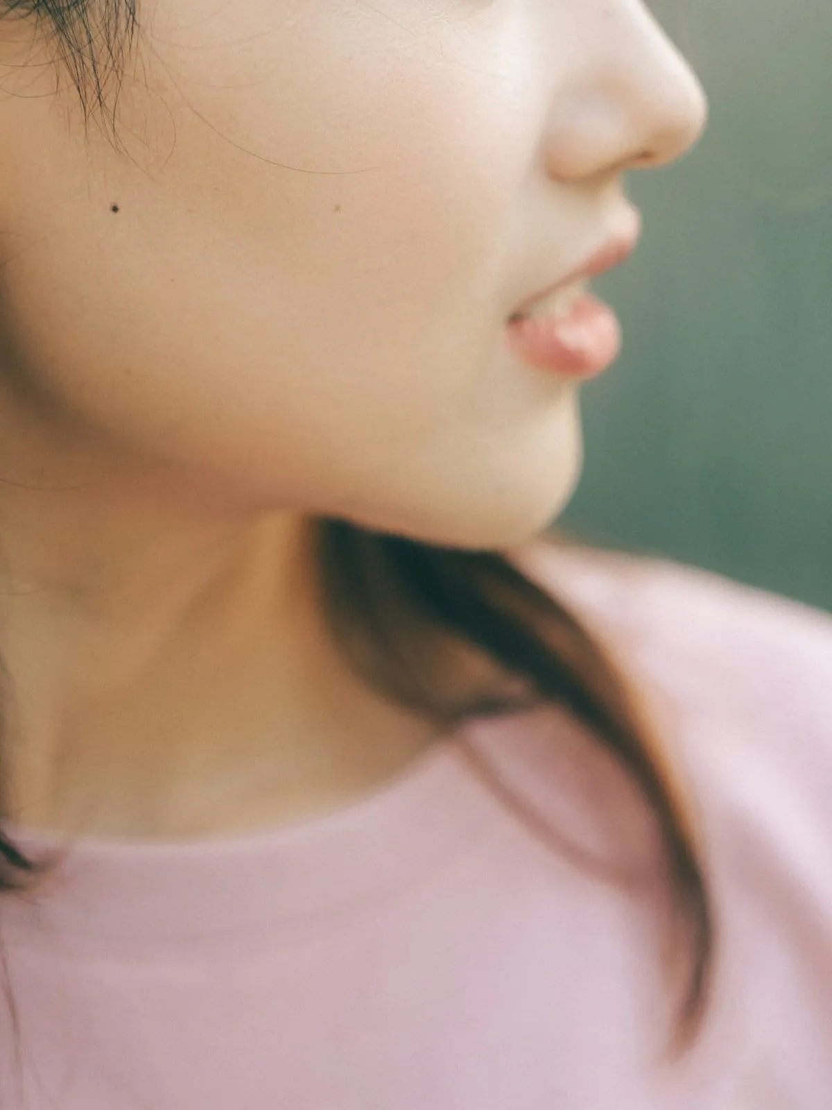 The lower half of a young woman’s face, turned to the side, above a pink T-shirt